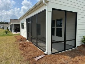 Completed custom screen enclosure by Express Sunrooms of Charleston in Del Webb Nexton. The photo shows the seamless integration of the screen room with the existing home's roofline and the transition to the new travertine paver patio in Summerville, SC.